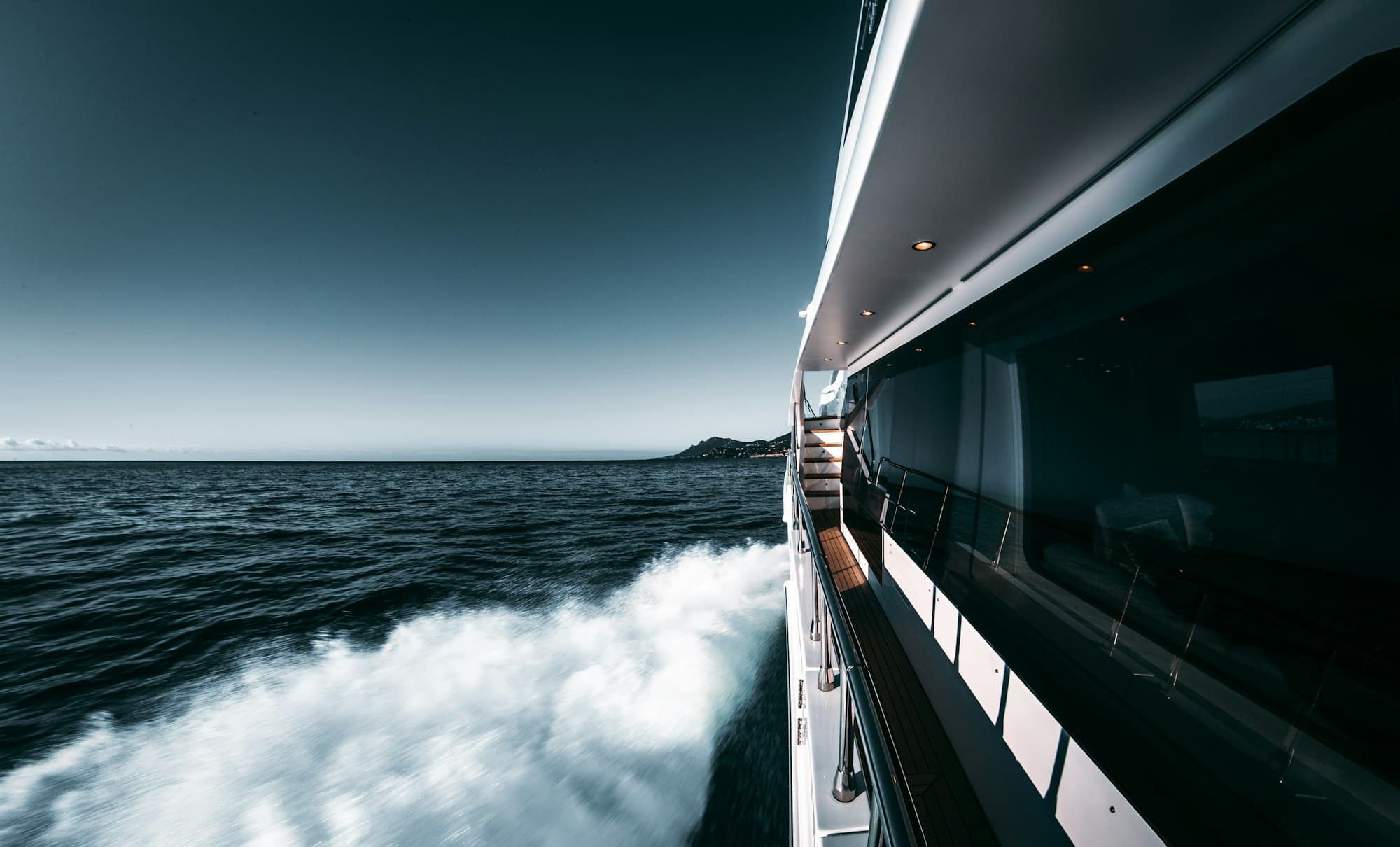 Superyacht underway at dusk off the coast, crew deck visible along the side rail